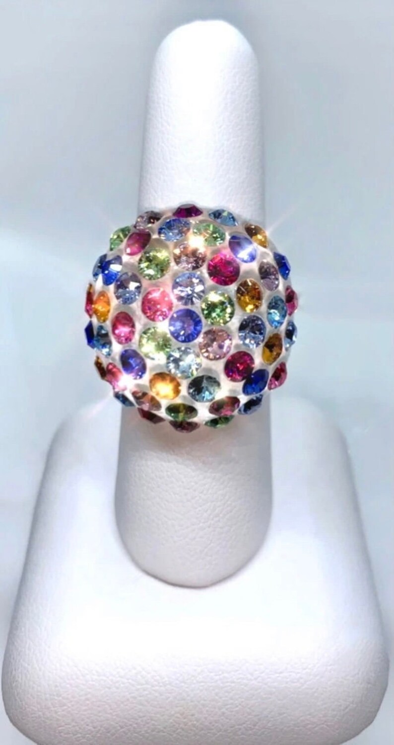 May include: A ring with a large, round, multi-colored gemstone. The gemstone is set in a silver band and is covered in small, round, colorful stones.