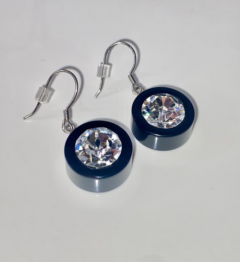 May include: A pair of black and silver earrings with a large clear crystal in the center of each earring.