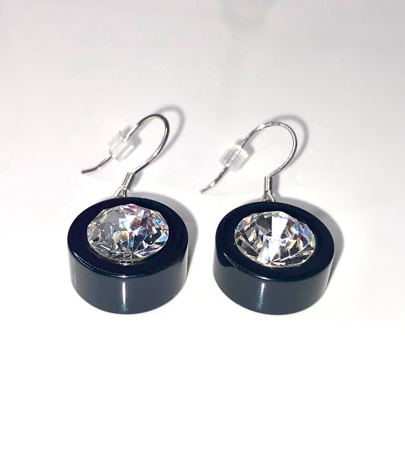 May include: A pair of black and silver earrings with a clear crystal in the center of each earring.