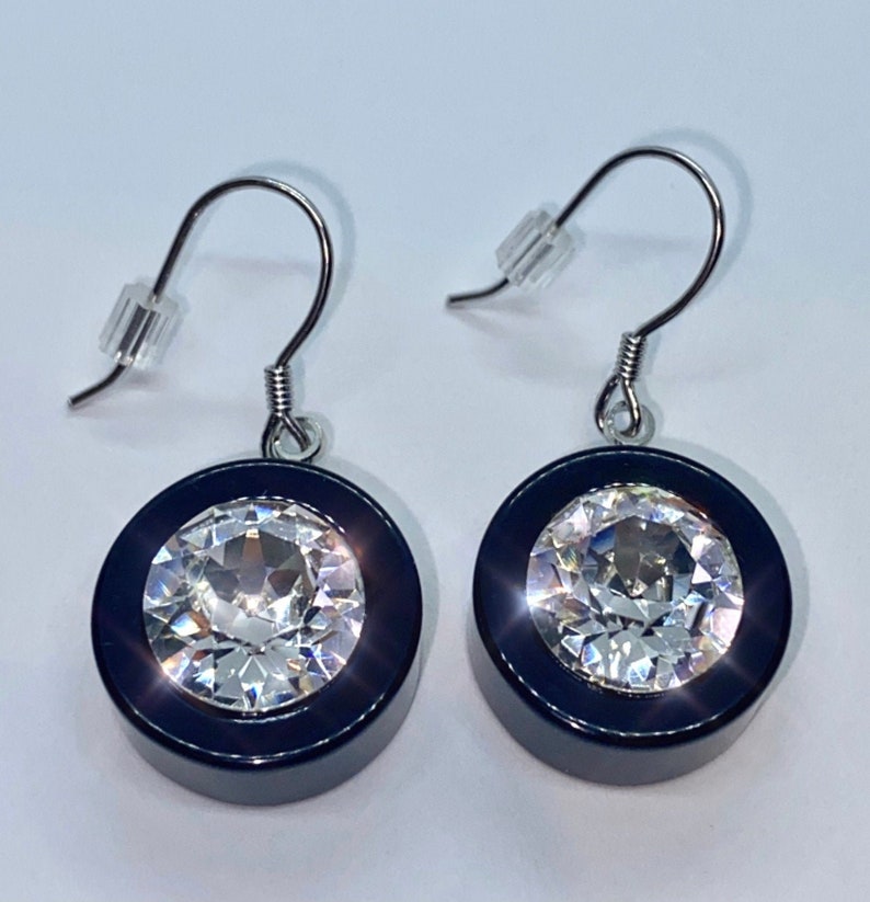 May include: A pair of silver dangle earrings with black and silver round pendants. Each pendant features a large clear crystal in the center.