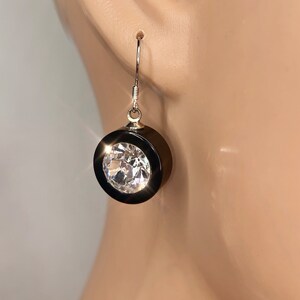 May include: A pair of dangle earrings with a black round setting and a clear crystal stone.