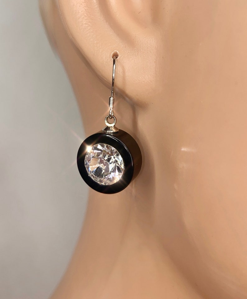 May include: A pair of dangle earrings with a black round setting and a clear crystal stone.