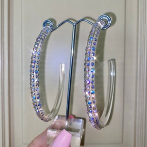 May include: A pair of large hoop earrings with clear acrylic hoops and iridescent rhinestones.