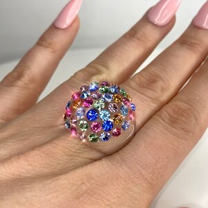 May include: A clear ring with a dome-shaped top covered in colorful rhinestones. The rhinestones are in shades of pink, blue, green, yellow, and orange.