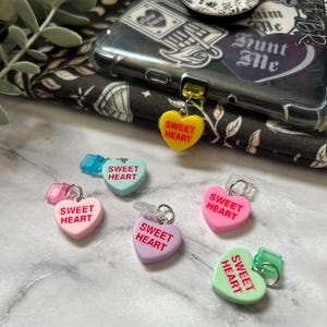 May include: Six heart-shaped charms with the text "Sweet Heart" in red letters. The charms are in various colors: yellow, light blue, pink, purple, and green.