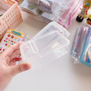 May include: A clear plastic storage container with a hinged lid. The container is divided into three sections.