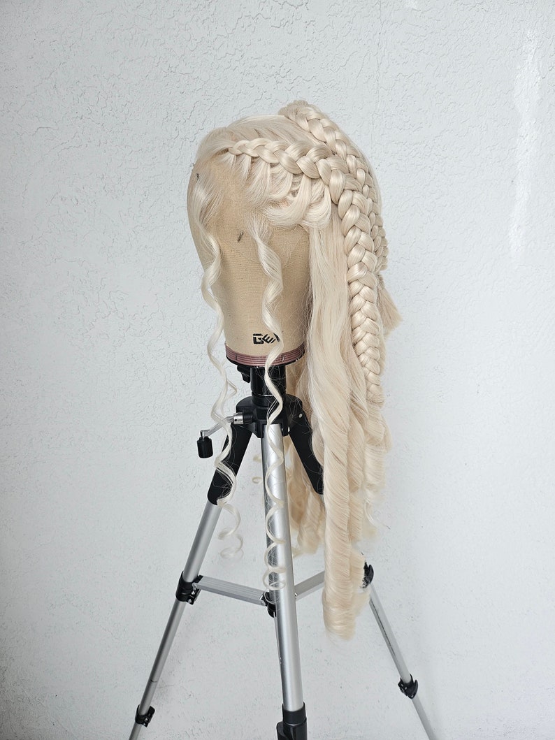 May include: A blonde wig with two braids styled on a mannequin head, mounted on a silver tripod.