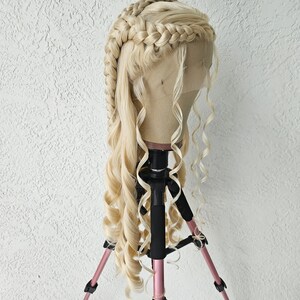 May include: A blonde wig with two braids and long, loose curls. The wig is on a tripod stand.