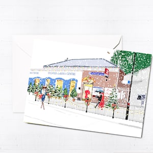Peut inclure: Une scène d'hiver enneigée avec un bâtiment qui dit "Dulwich Garden Centre" et "Christmas Shop" avec des gens qui passent. Il y a des sapins de Noël et des décorations devant le bâtiment.