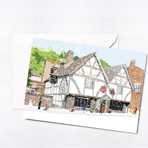 May include: A snowy winter scene with a white building with black trim and a sign that reads "The Old House." The building has a festive feel with Christmas lights and wreaths. There are people walking in front of the building.