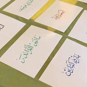 May include: A collection of white cards with Arabic calligraphy in different colors, including blue, green, and red. The text on the cards includes the words "Maatiq Al-Kazand", "Jaman Jaman", "Mary Katerine", "Daroo Josif", and "Amada Mary".