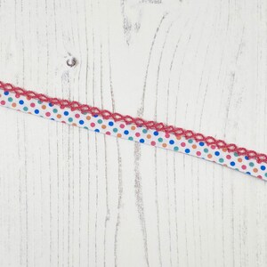Peut inclure: Un ruban blanc à pois rouges, bleus et orange. Le ruban a une bordure en crochet rose.