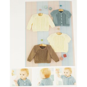 May include: Four knitted baby sweaters in different colors: brown, yellow, light blue, and a darker blue. The sweaters have a lace pattern and button closures. Three of the sweaters are hanging on hangers, while the fourth is lying flat. The sweaters are displayed on a striped background.