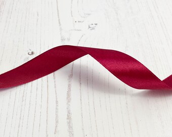 May include: A close-up of a burgundy satin ribbon on a white wooden surface.