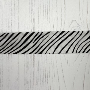 May include: A black and white zebra print fabric ribbon against a white woodgrain background.