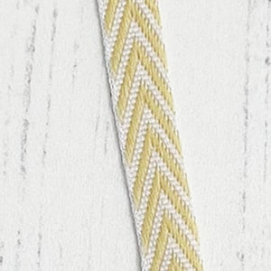 May include: A close-up of a yellow and white chevron ribbon. The ribbon is woven with a herringbone pattern.