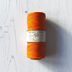 May include: A spool of orange hemp cord with a label that reads "HEMP CORD PREMIUM QUALITY Hemptique".