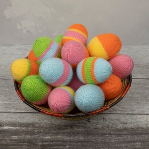 May include: A basket filled with colourful knitted Easter eggs. The eggs are in shades of pink, blue, green, yellow and orange.
