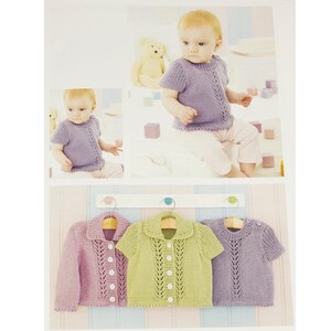 May include: Three knitted baby cardigans in different colors: pink, green, and purple. Each cardigan has a button closure and a lace pattern.