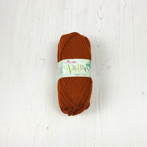 May include: A ball of brown super chunky yarn, labelled "kingcole big Value". The yarn is a warm, earthy tone, suitable for knitting or crochet. The background is a white wooden surface.