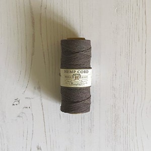 Può includere: Un rotolo di corda di canapa marrone con un'etichetta che recita "Hemp Cord, Premium Quality, Hemptique".