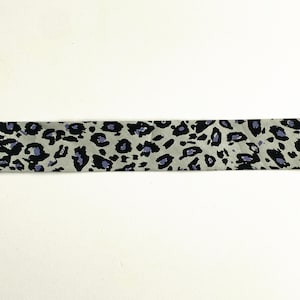 Pode incluir: Um close-up de um tecido cinza e preto com um padrão de estampa de leopardo. O tecido tem um tom roxo sutil.