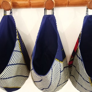 Può includere: Tre cesti portaoggetti in tessuto appesi con tessuto a righe blu e bianche e dettagli gialli. I cesti sono appesi a un'asta di legno.