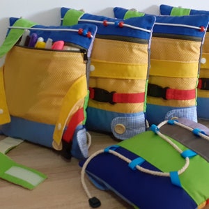 Peut inclure: Plusieurs coussins sensoriels colorés pour enfants. Chaque coussin présente différentes textures : fermetures éclair, boutons, boucles et attaches auto-agrippantes. Les couleurs dominantes sont le bleu, le jaune, le vert et le rouge.