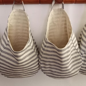 Pode incluir: Quatro sacos de armazenamento pendurados com um padrão listrado em preto e branco. Os sacos são feitos de um tecido macio e natural e são perfeitos para organizar pequenos itens.
