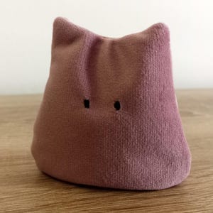Peut inclure: Un jouet en peluche rose en forme de blob avec deux yeux noirs.