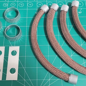 Peut inclure: Quatre tuyaux flexibles en métal tressé de couleur cuivre avec des embouts filetés argentés, trois petits anneaux circulaires argentés à bords striés et trois bandes adhésives rectangulaires blanches avec des découpes circulaires.