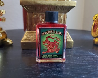 May include: A small glass bottle of red liquid with a black cap. The label is green and features a red dragon with the text "Dragon's Blood Oil" and "Lucky Mojo Curio Co."