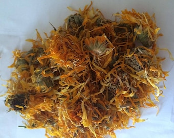 May include: Dried calendula petals, a vibrant orange-yellow color, are piled together in a loose heap. The petals are dried and have a slightly wrinkled texture.