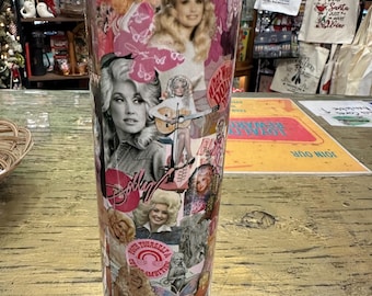 Puede incluir: Un vaso de acero inoxidable con un collage de imágenes de una mujer rubia, con la palabra "Dolly" en una fuente de escritura. El diseño incluye mariposas rosas y el texto "Pour Yourself A Little Ambition".