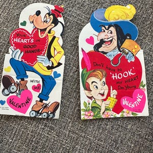 May include: Two vintage Valentine's Day cards featuring Disney characters. One card shows Goofy holding a heart with the text "Your heart's in good hands." The other card features Captain Hook and Peter Pan with the text "Don't have to hook my heart, I'm yours."