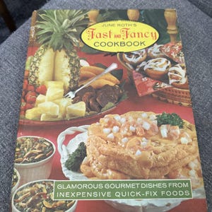 以下が含まれることがあります： June Roth's Fast and Fancy Cookbookというタイトルの料理本。サブタイトルはGlamorous Gourmet Dishes from Inexpensive Quick-Fix Foods。表紙にはパイナップル、料理の皿、エビ料理が赤い背景に描かれています。
