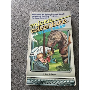 May include: A paperback book titled Micro Adventure no. 4 Time Trap by Jean M. Favors. The cover features a large brown dinosaur, two people in a forest, and a futuristic vehicle. The top text reads More Than An Action-Packed Novel! Includes 6 Exciting Programs For Your Computer!
