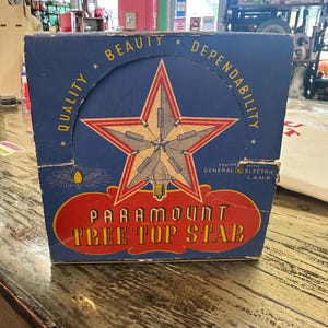 Könnte beinhalten: Vintage Karton für einen Paramount Tree Top Star. Die Box ist blau mit einem großen Stern-Design in Rot, Gold und Weiß. Der Text enthält "Qualität, Schönheit, Zuverlässigkeit" und "General Electric Lampe".