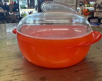 Peut inclure: Un plat à casserole Pyrex orange avec un couvercle en verre transparent. Le plat a deux poignées latérales et une poignée sur le couvercle. Le plat est posé sur une surface en bois.
