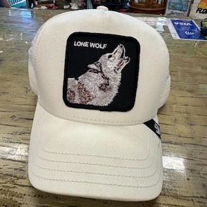 May include: A cream-colored baseball cap with a mesh back and a curved brim. The front features a black square patch with the words "LONE WOLF" above a howling wolf illustration. The cap is designed with a classic six-panel construction.