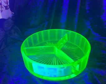 May include: A round, divided serving dish in a vibrant neon green color. The dish is made of glass and has three sections, with a starburst design in the center. The rim has vertical lines. The background is a dark blue.
