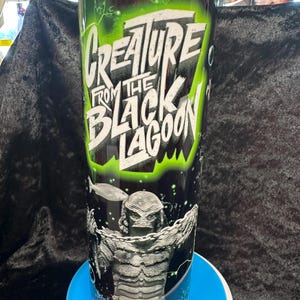 May include: A tall tumbler featuring the text "Creature From The Black Lagoon" in white and neon green. The design includes an illustration of the Creature from the Black Lagoon in black and white.