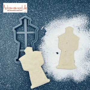 Könnte beinhalten: Ein grauer Plastik-Ausstecher in Form eines Leuchtturms, mit einem weißen Keks, der mit dem Ausstecher ausgestochen wurde. Der Ausstecher und der Keks befinden sich auf einer grauen Oberfläche mit weißem Puderzucker.