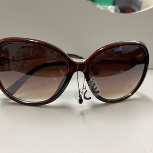 May include: Brown oval-shaped sunglasses with brown lenses. The sunglasses have a tag that says "UV 400 CE".