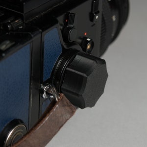May include: Close-up of a black camera with a blue leather strap and a black lens cap. The camera has a silver knob and a black dial.