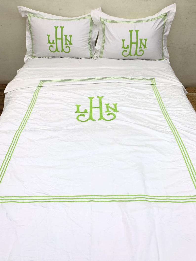 Puede incluir: Juego de cama blanco con ribete bordado y monograma en verde. El juego incluye dos fundas de almohada y una funda n&oacute;rdica, todo con una est&eacute;tica limpia. El bordado verde proporciona un toque de color sobre la tela blanca.