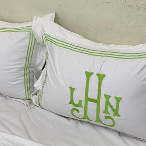 Puede incluir: Dos fundas de almohada rectangulares blancas con iniciales bordadas en verde y ribete verde. Las iniciales "LHN" se muestran en la parte delantera de cada almohada. Las fundas de almohada est&aacute;n sobre una s&aacute;bana blanca.