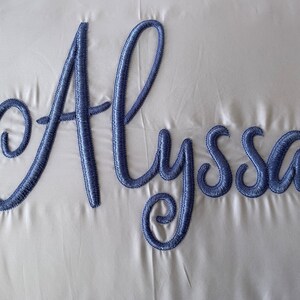 May include: A white pillow with the name "Alyssa" embroidered in blue cursive lettering.