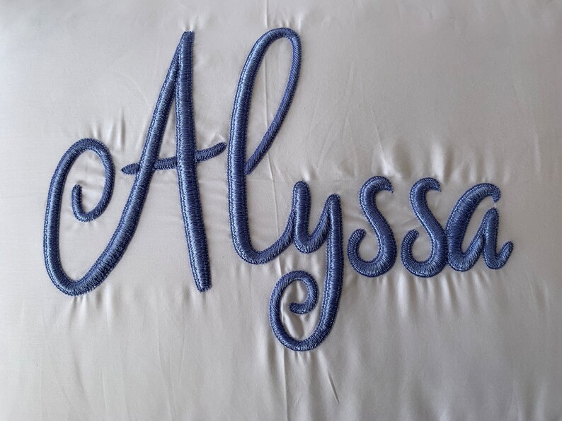 May include: A white pillow with the name "Alyssa" embroidered in blue cursive lettering.