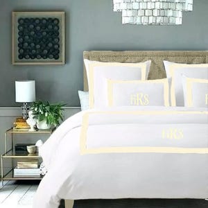 May include: White bedding with a cream colored border and the monogram "FKS" embroidered on the pillow and duvet cover.